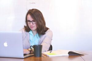 Focused businesswoman using a laptop at a desk with a mug and open notebook.